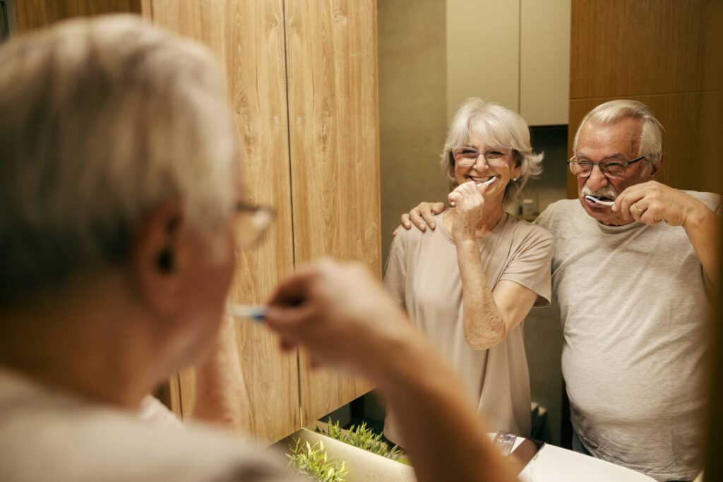 Reflection in the mirror of senior couple brushing their teeth with toothbrushes in bathroom in the morning.